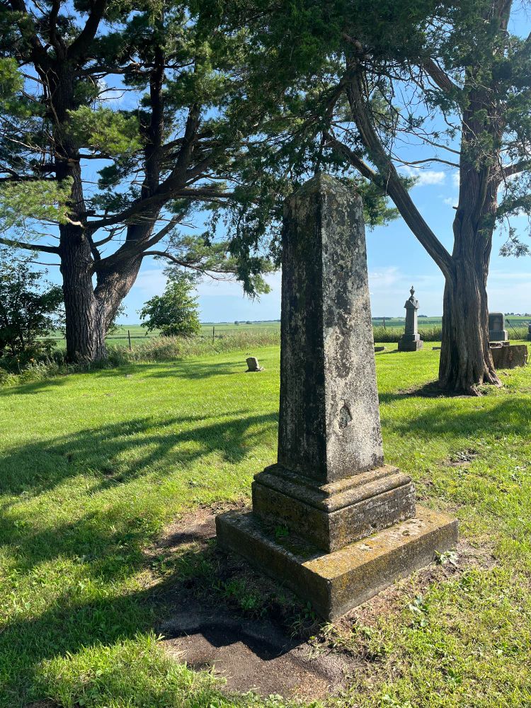 A rural cemetery with a weathered stone obelisk with no legible markings. 