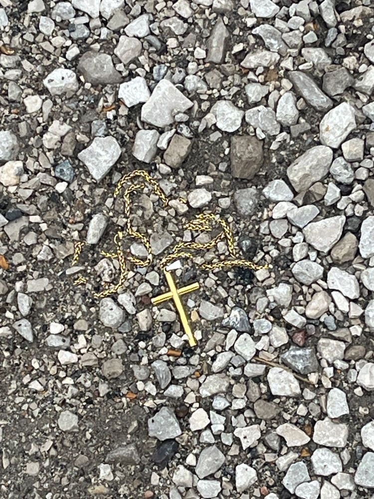 Outside the cemetery grounds, beside the road, in the gravel, was a crucifix on a gold chain, pressed into the dirt. 