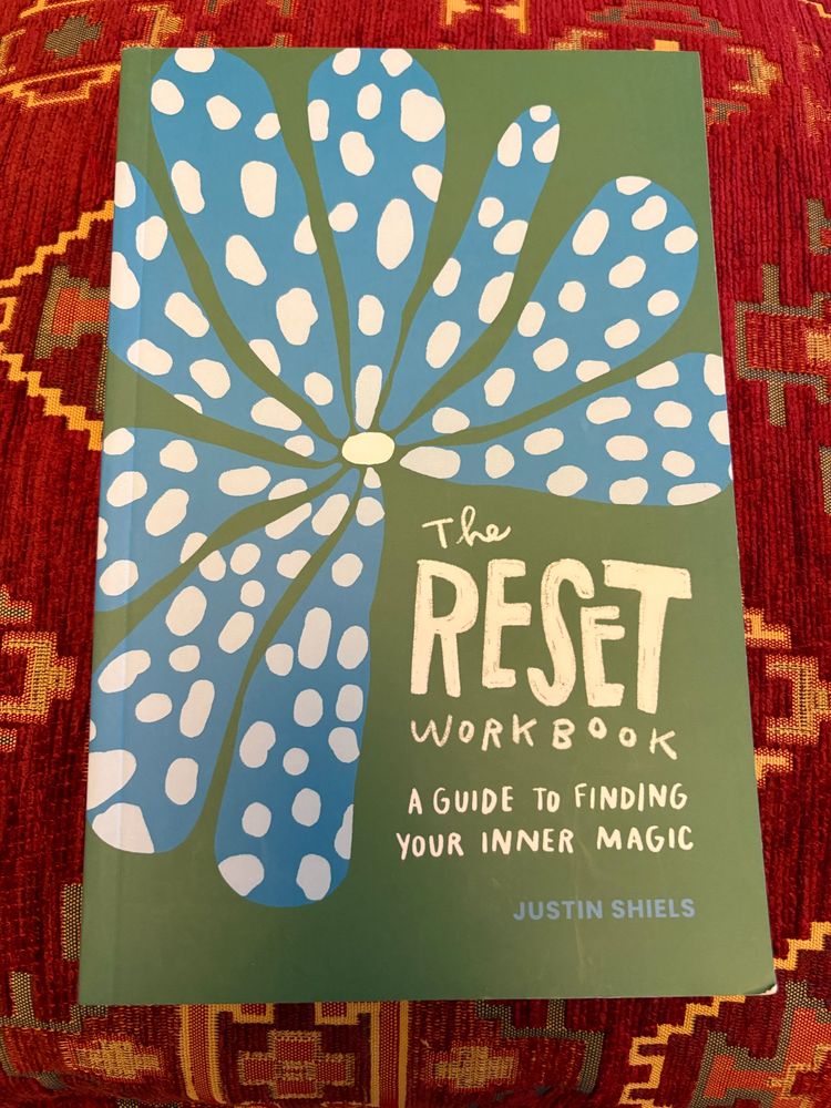 Cover of a book: The Reset Workbook by Justin Shiels. Cover is green with a drawing of a blue and white flower. 