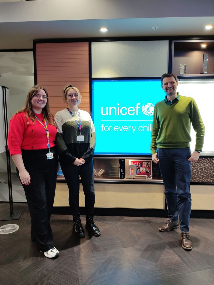 Abigail, Amy and James standing in front of an illuminated UNICEF UK sign