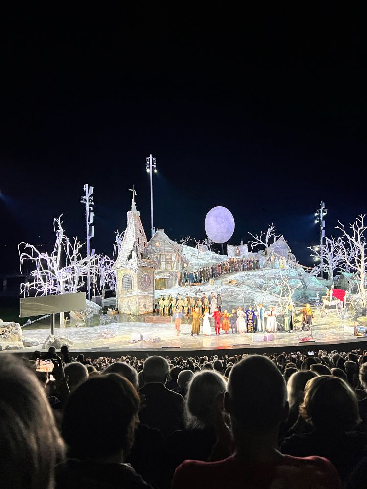 Seebühne Bregenz bei Nacht .
Vordergrund Publikum
Hintergrund Berge und Himmel
Bühnenbild: Kirchturm, Schneelandschaft , Vollmond
Am Bühnenrand die Darsteller beim Schlussapplaus