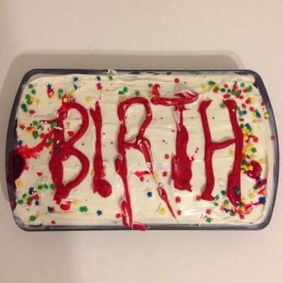 A very ominous looking sheet cake that has white frosting, rainbow sprinkles and "BIRTH" written in red frosting in a sloppy way.