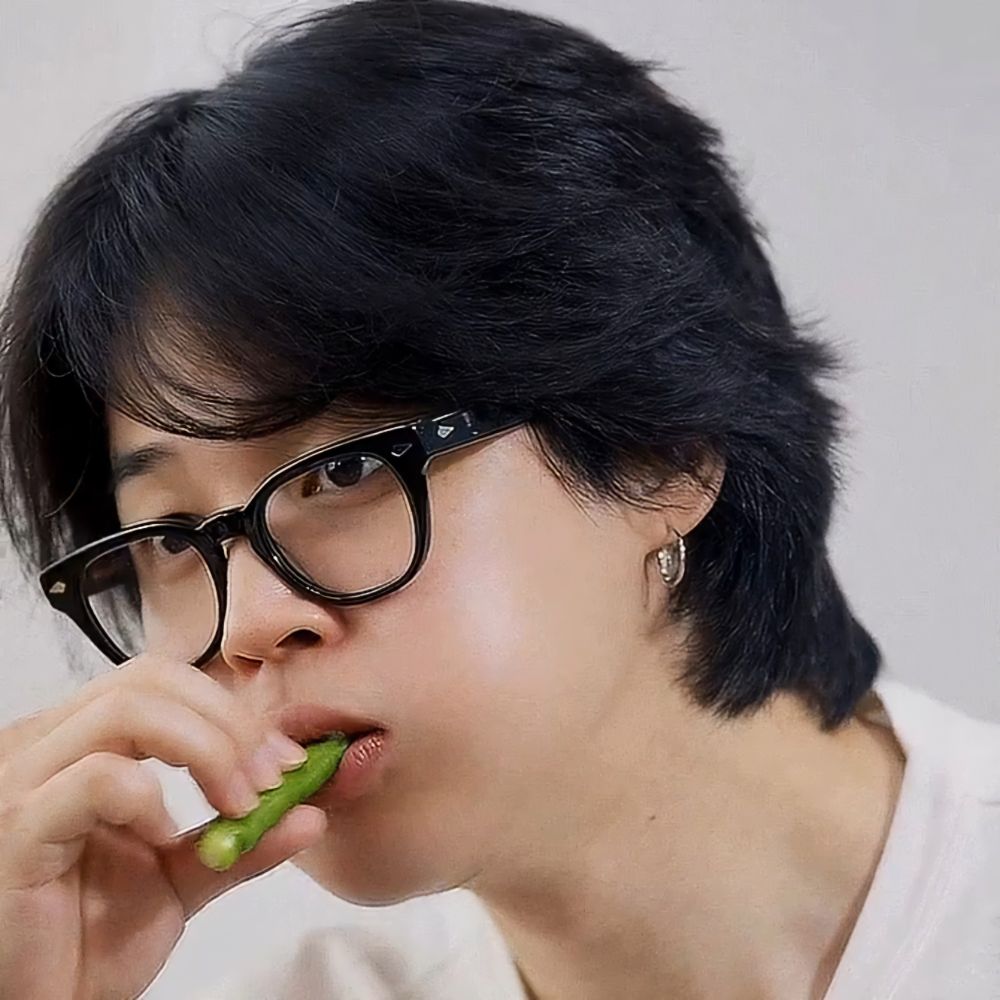Jimin with dark hair is wearing glasses with a black frame