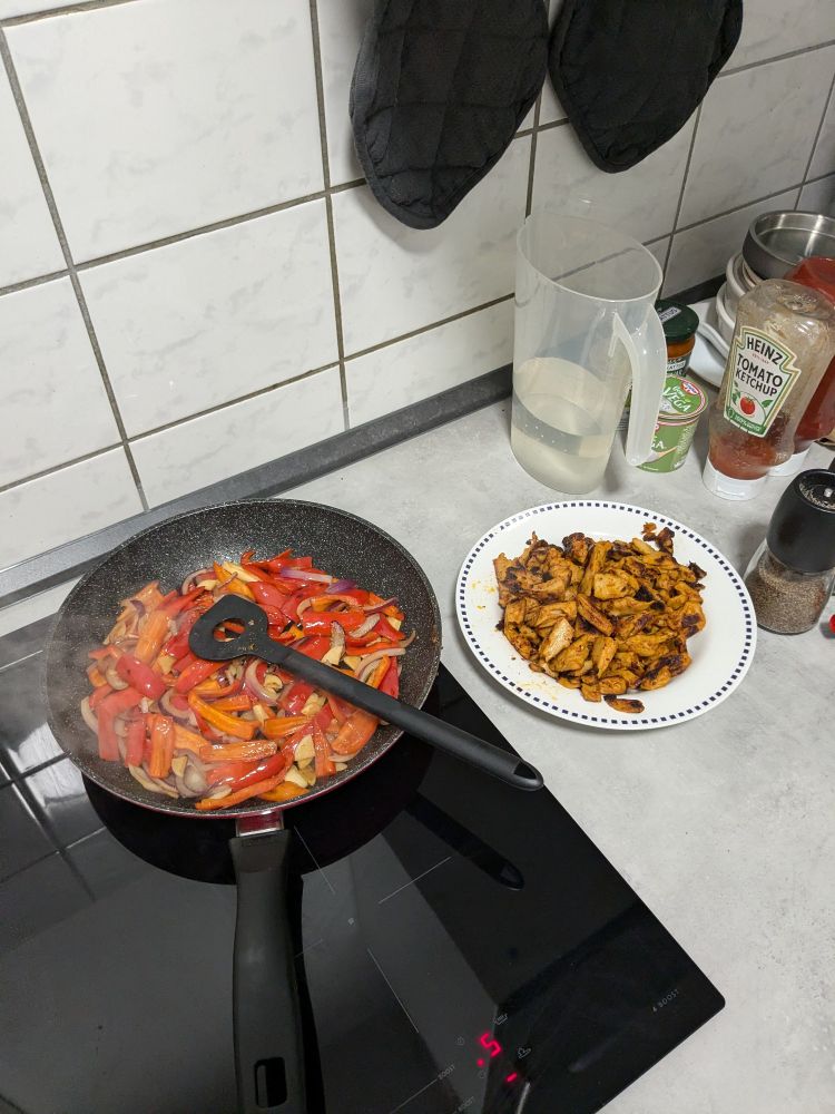 Zweite Arbeitsstufe mit angebratenem veganen Hähnchenstücken in einem Teller und Gemüse in der Pfanne wird angebraten 