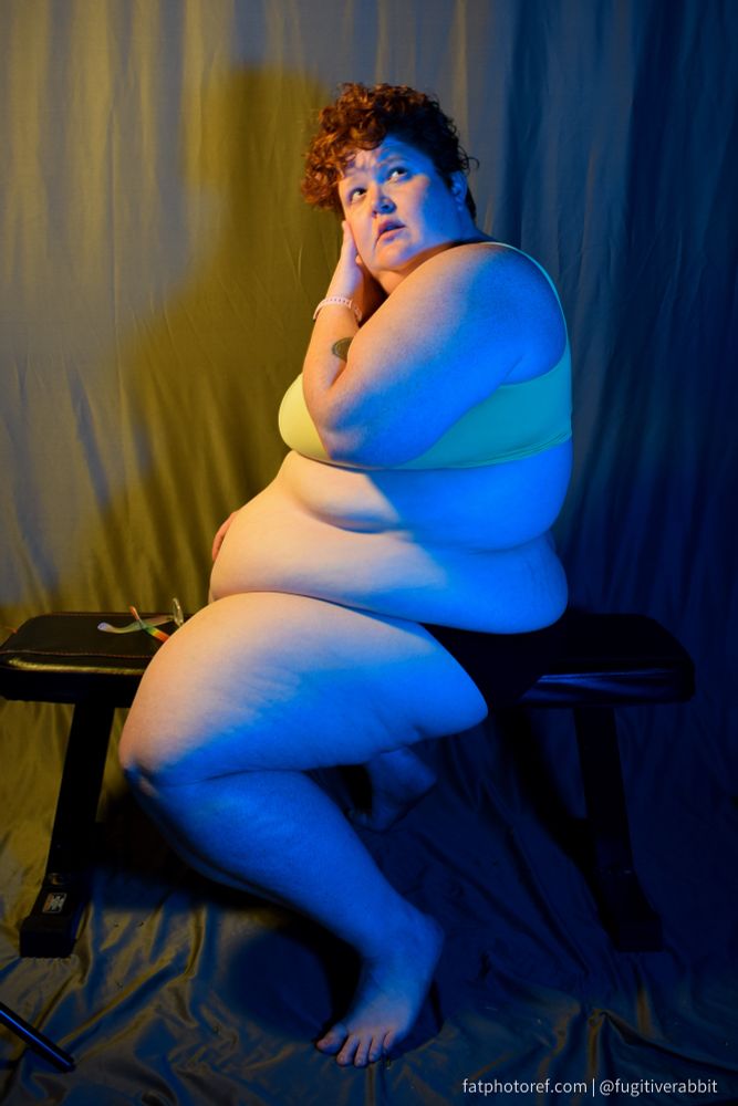A fat woman sitting sideways on a bench with yellow and blue lighting 
