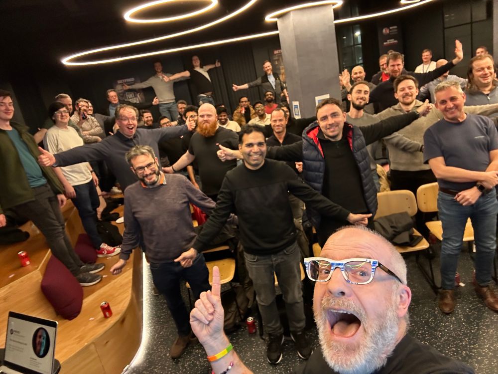 Jim smiling and pointing to an audience at an event. The audience are stretching their arms