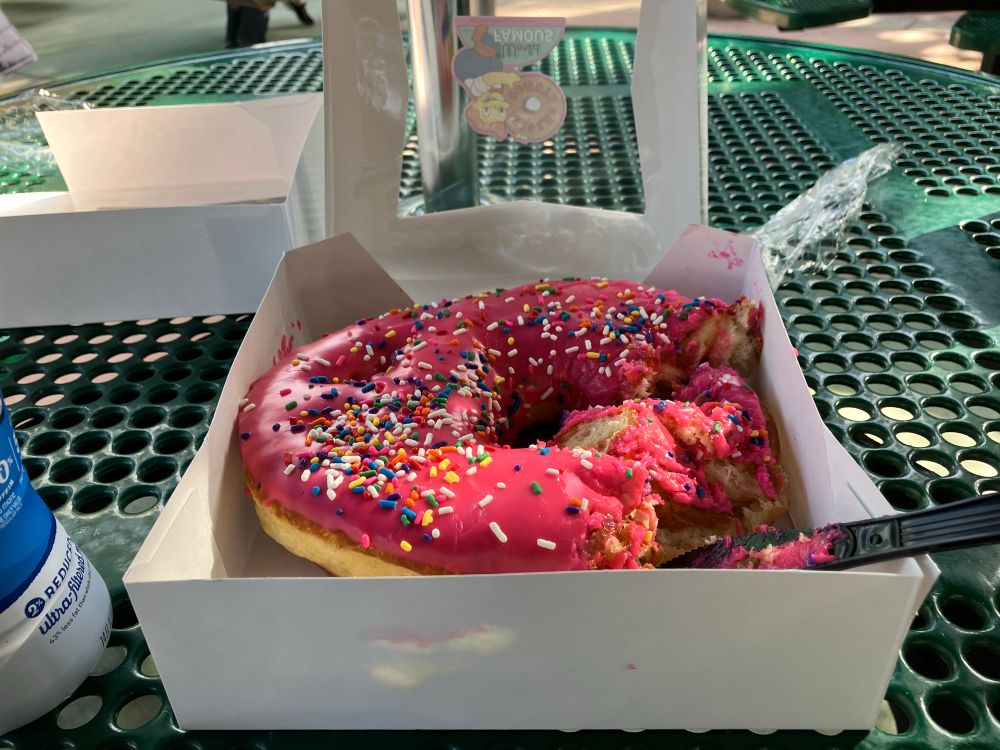 A very big donut with pink frosting and sprinkles from The Lard Lads Donuts Shop.