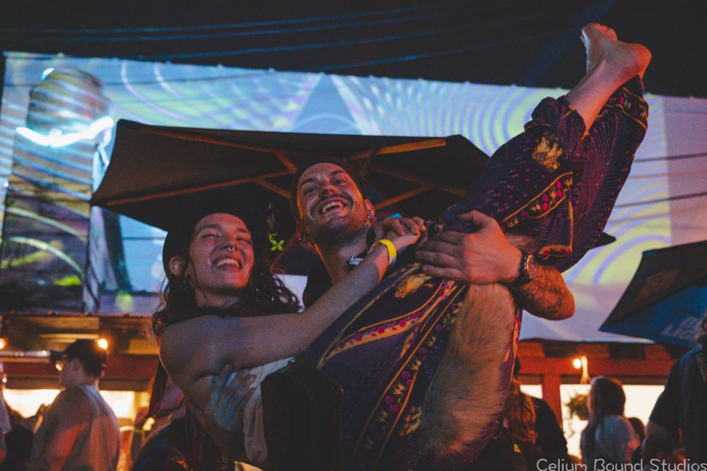 A happy couple asked me If I wanted a good photo, then posed for this. He is holding her in his arms, big grins, and some digital visual art behind them. 