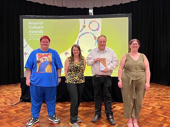 Image of Jodie Bradley, Amy Russell, Gary Bourlet and Vicky Farnsworth on a stage. Gary is holding an award. Behind them a screen reads research culture awards 2024.