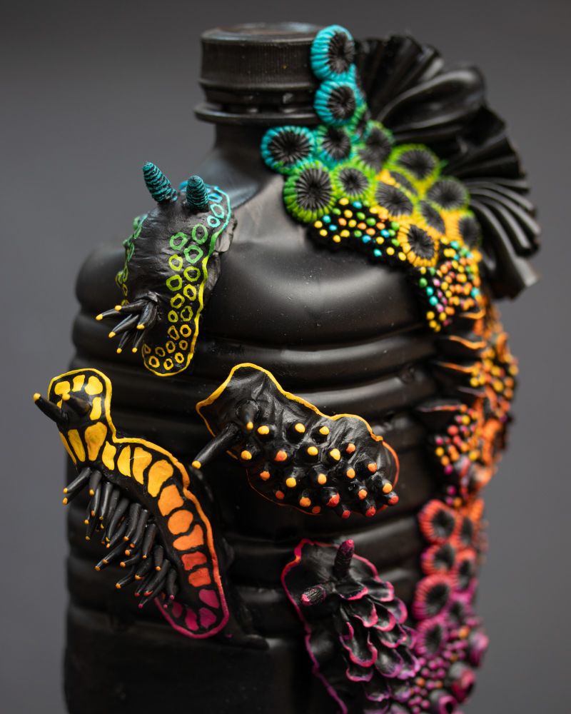 Nudibranches and coral reef sculptures on a black plastic bottle. The slugs and reef are also painted in black as a base and adorned with rainbow colors.