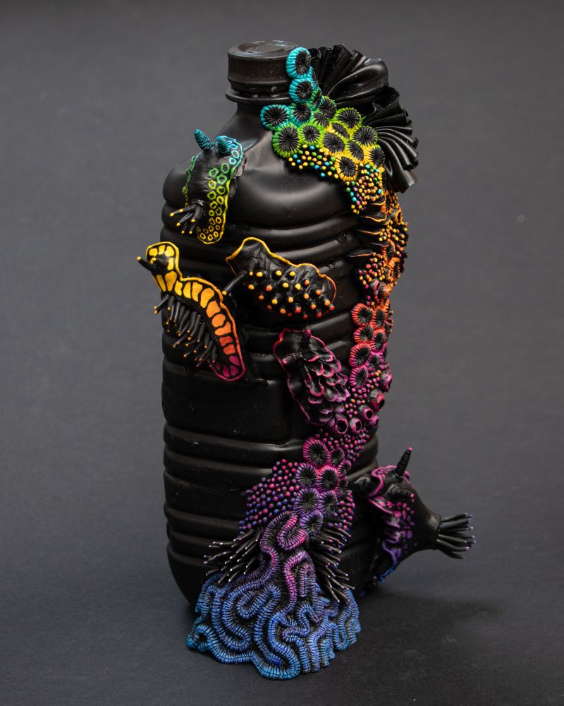 Nudibranches and coral reef sculptures on a black plastic bottle. The slugs and reef are also painted in black as a base and adorned with rainbow colors.