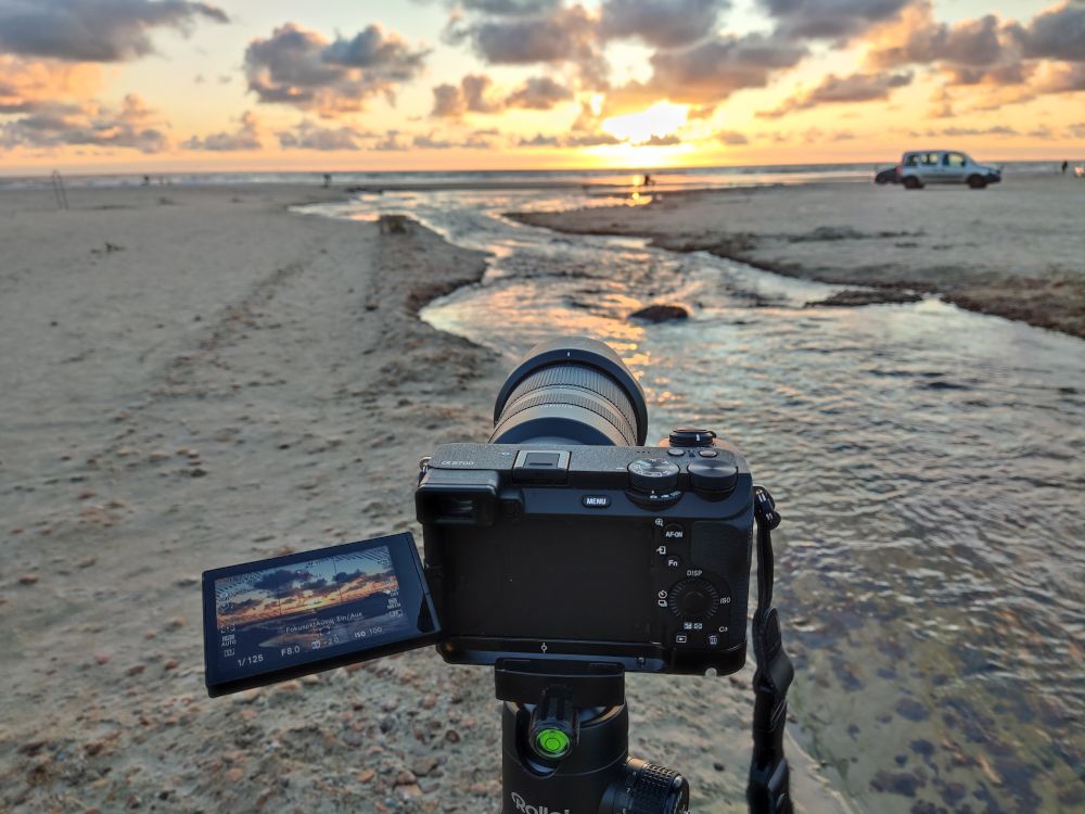 Abendstimmung am Strand. Im Vordergrund eine Kamera mit Schwenkdisplay 