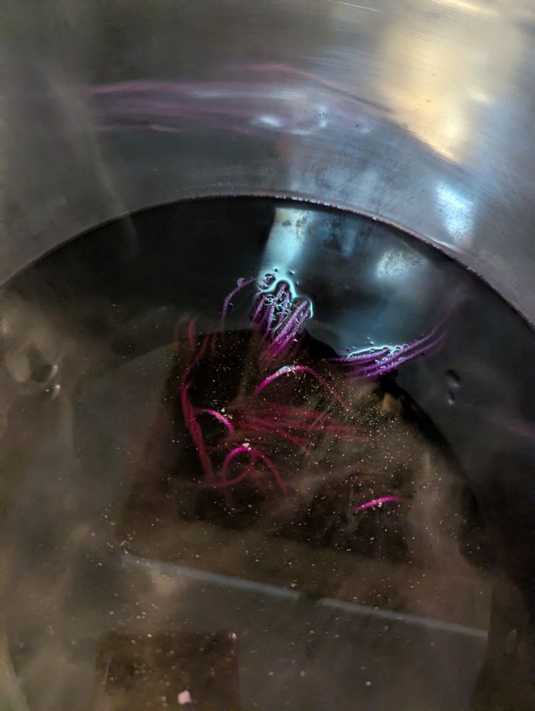 Strands of yarn barely visible in a dark dye bath with hints of fuschia and purple.