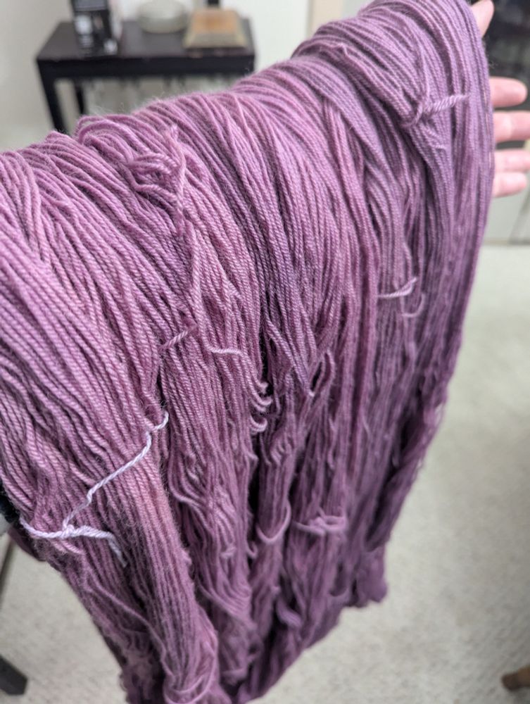 A group of skeins of yarn suspended in order of deepening shades of mauve.