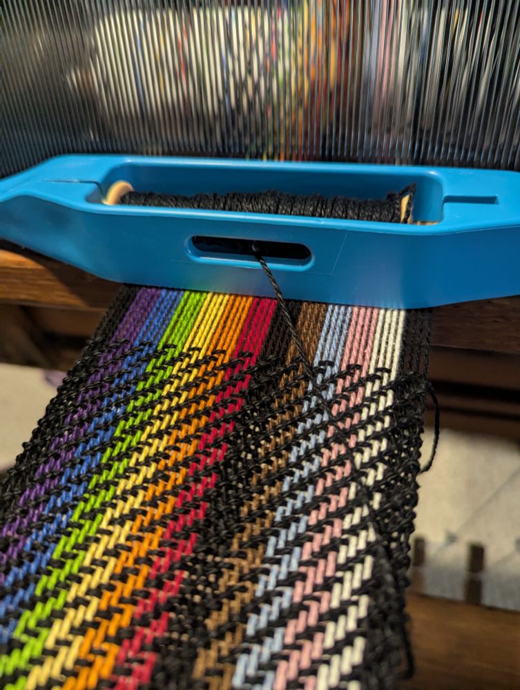 2x2 twill with a striped warp of black, purple, blue, green, yellow, orange, red, black, brown, light blue, pink, white, and black with blue shuttle holding black weft.