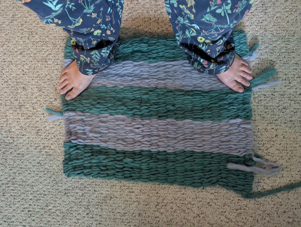 Rug of 3 seafoam green stripes against 2 pale gray stripes. Human wearing Duluth overalls in wildflower navy print standing on the top of the rug for scale.