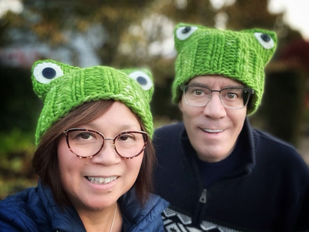 Two people wearing green knit hats featuring frog eyes 