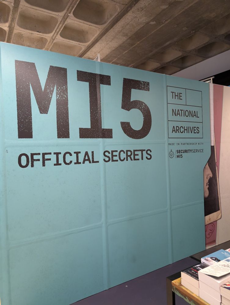 The entry artwork for the MI5 Official Secrets exhibition at the National Archives at Kew. The background is a blue colour and the title text and credits are in black. 