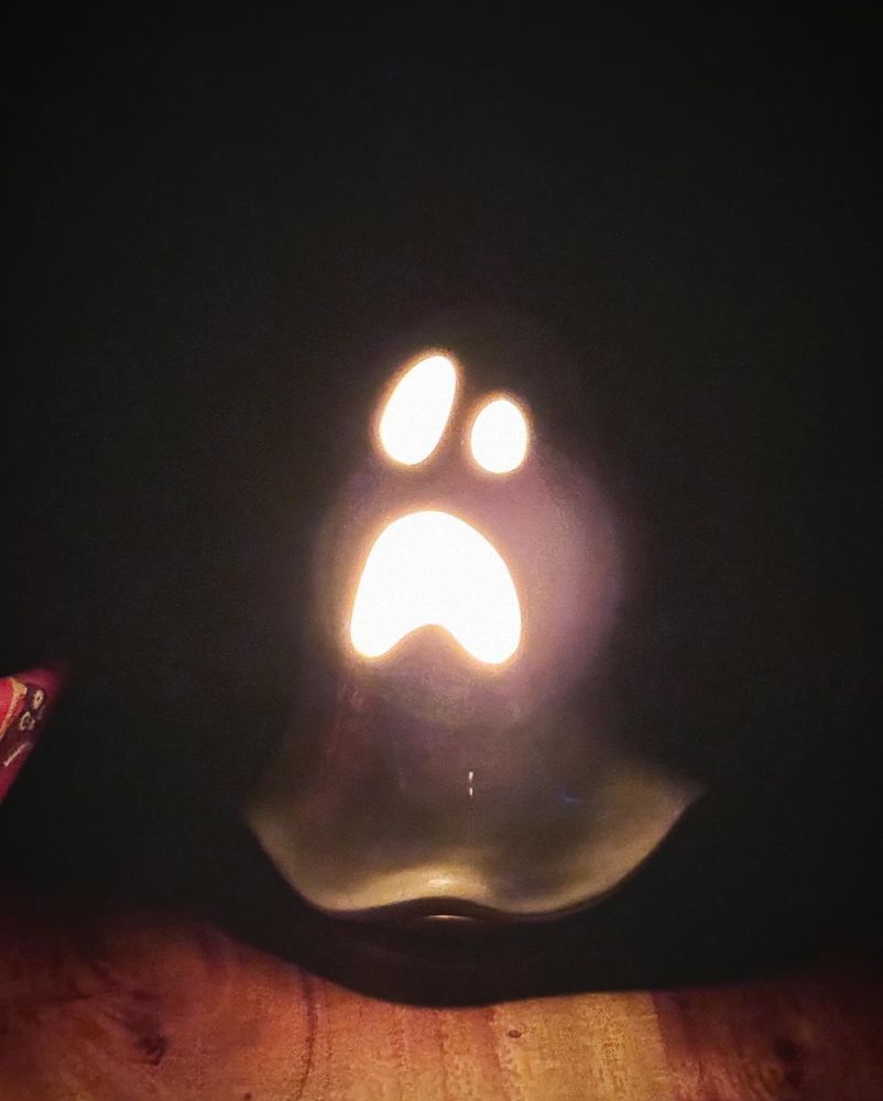 Image of a white ceramic ghost lit up from within, shining brightly through its eyes and mouth in a dark room. 