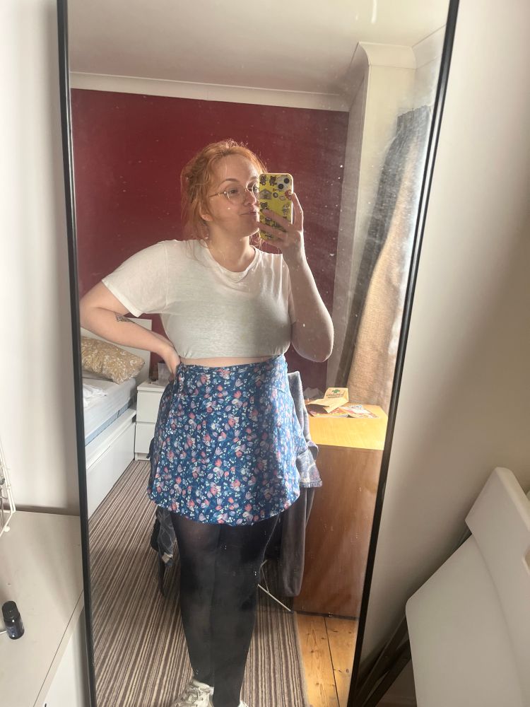 I’m taking a mirror selfie while wearing a white t shirt and wrap skirt with blue flower pattern.