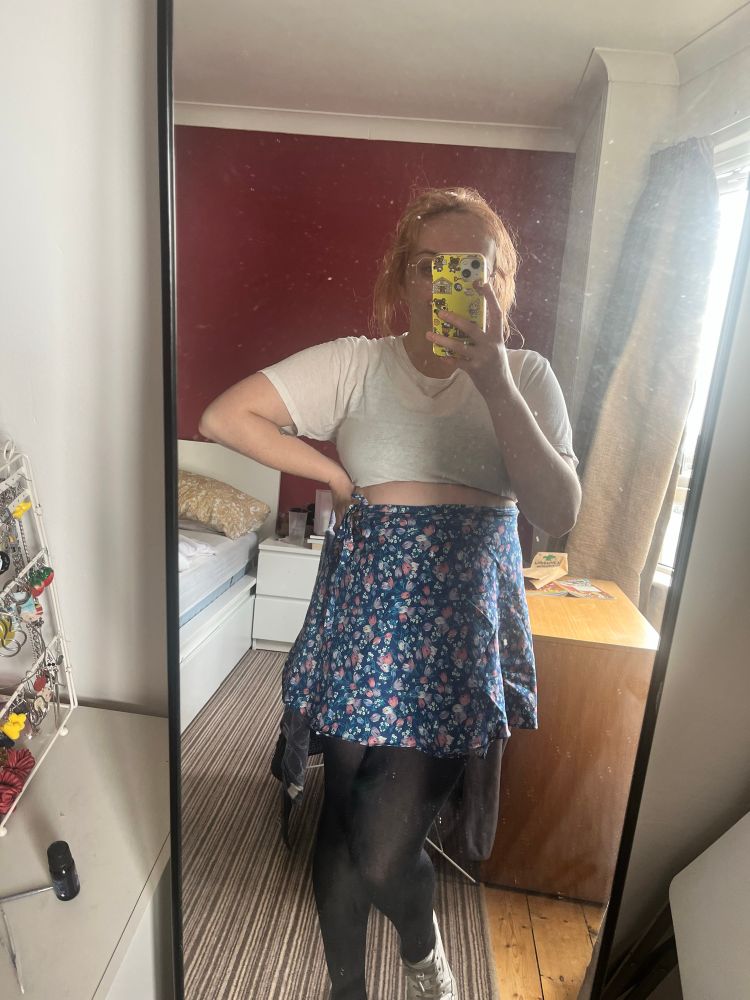 I’m taking a mirror selfie while wearing a white t shirt and wrap skirt with blue flower pattern.