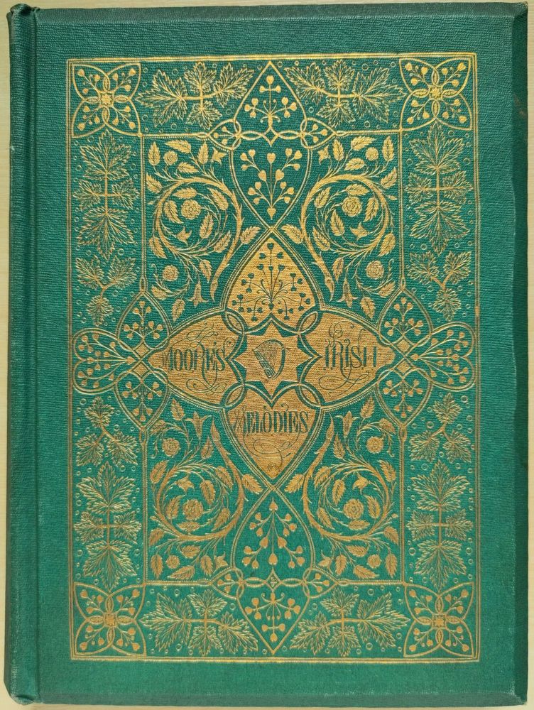 Photograph showing the front cover of Moore's Irish Melodies (1866), which is a vivid green with golden decoration of a small harp in the centre, enclosed by four interlocking hearts featuring the book's title, and surrounded by swirling leaves and flowers.