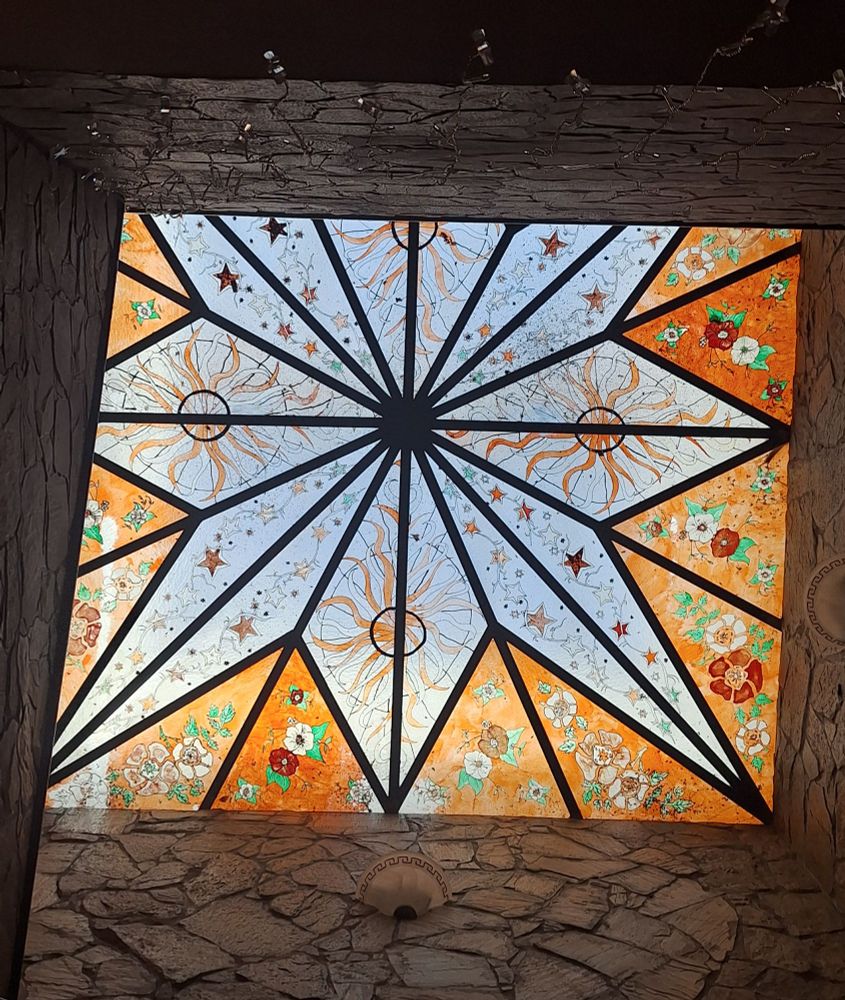 foto desde abajo a la vidriera del techo. con figuras geométricas, soles y flores de cristales de colores