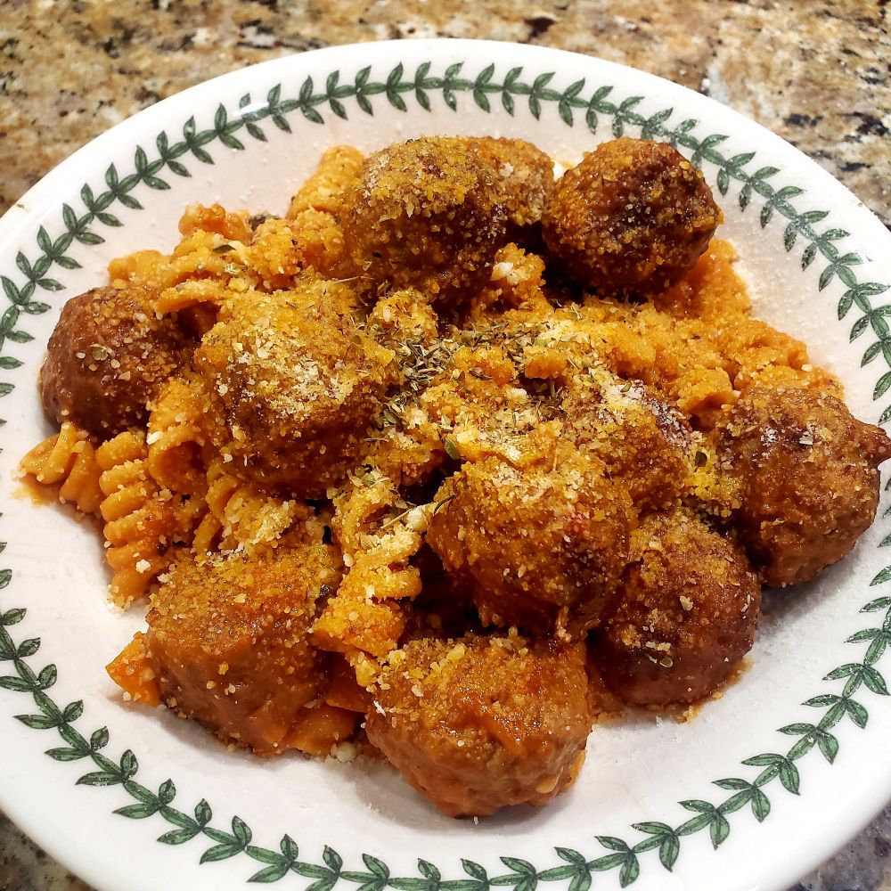 A bowl of pasta & meatballs sprinkled with freshly grated parmesan