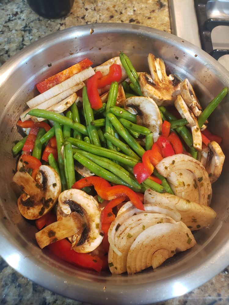 A stainless steel prep bowl filled to the brim with marinating veggies