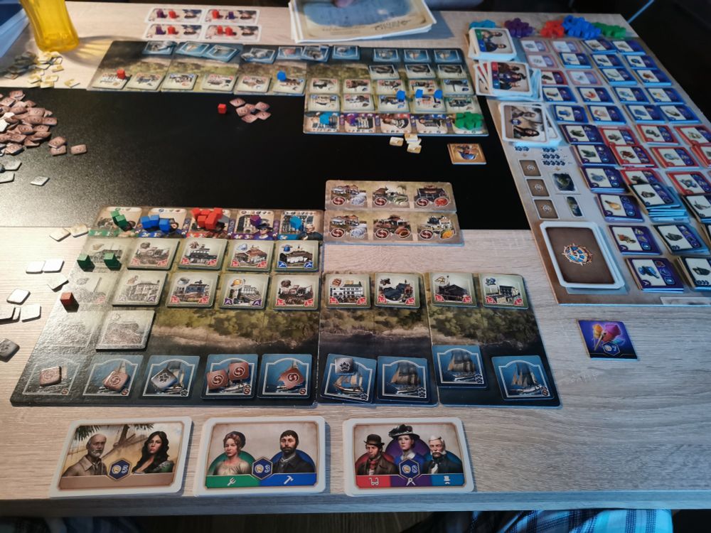 Man sieht ein Spielbrett mit diversen Karten und Klötzchen.
Die Bilder der Menschen auf den Karten sind an das 1800 Jahrhundert angepasst. Es sind zudem Schiffe und diverse Gebäude erkennbar