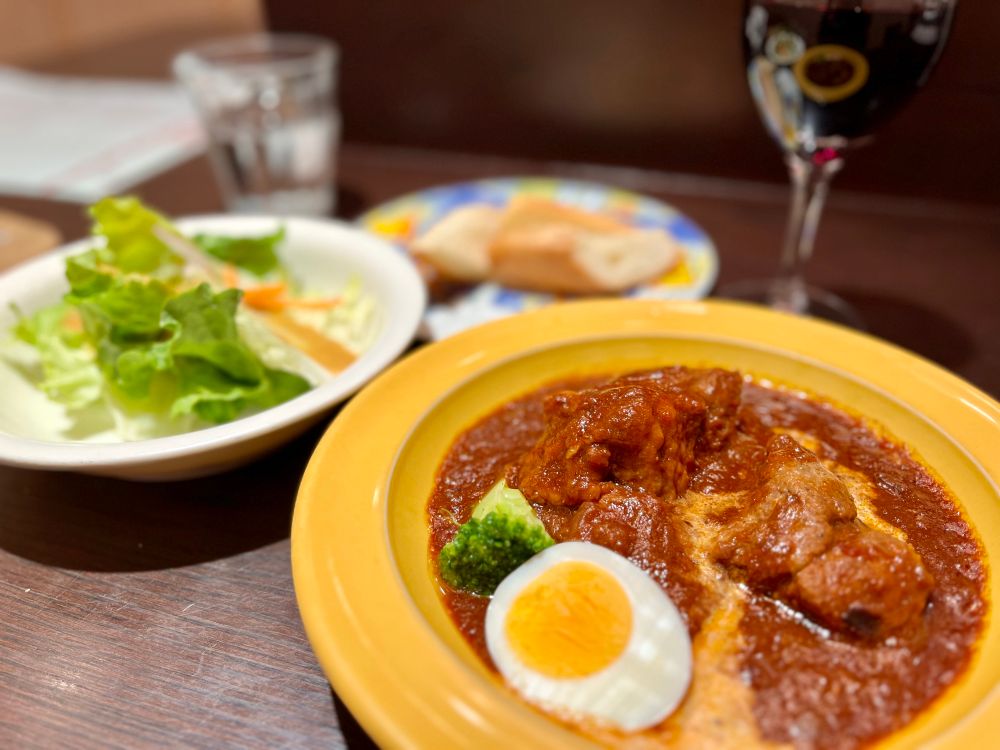 アンガスビーフシチューにサラダとパンと赤ワインの写真。