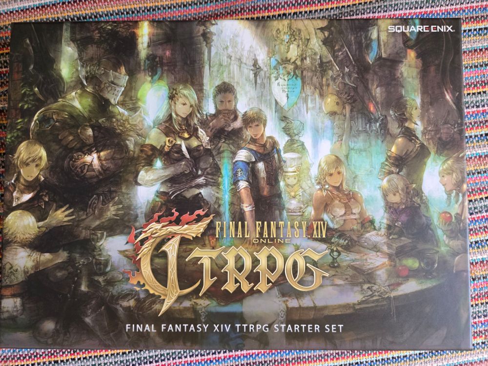 A imagem mostra a capa do Final Fantasy XIV Online TTRPG Starter Set, um conjunto inicial para RPG de mesa baseado no jogo online da Square Enix. A arte apresenta um grupo diversificado de personagens icônicos do universo de Final Fantasy XIV reunidos em uma sala iluminada por luz suave. À esquerda, um personagem com armadura pesada está em pé, enquanto à direita outros personagens, incluindo uma miqo'te, estão ao redor de uma mesa decorada com alimentos, bebidas e objetos de RPG. O título "Final Fantasy XIV Online TTRPG" está em destaque na parte inferior, com o logotipo da Square Enix no canto superior direito. A composição evoca um clima de aventura e camaradagem.


