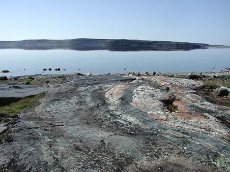 Colorful rocks in front of a cove with some land behind it.  This is an outcrop of metamorphosed volcano-sedimentary rocks from the Porpoise Cove locality, Nuvvuagittuq supracrustal belt, Canada.   

From here:

https://commons.wikimedia.org/wiki/File:Nuvvuagittuq_belt_rocks.jpg