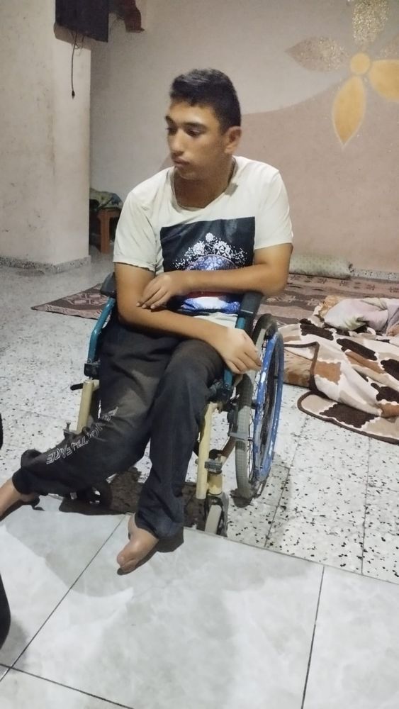 a teenage boy, Ahmed, sits in a wheelchair, with his injured and paralyzed legs awkwardly positioned