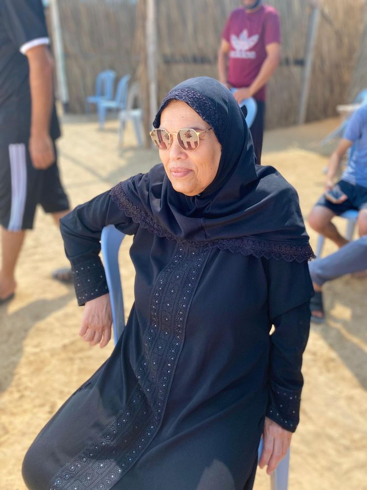 a woman, Fatima, is sitting in a chair outdoors, wearing glasses and a black dress and headscarf