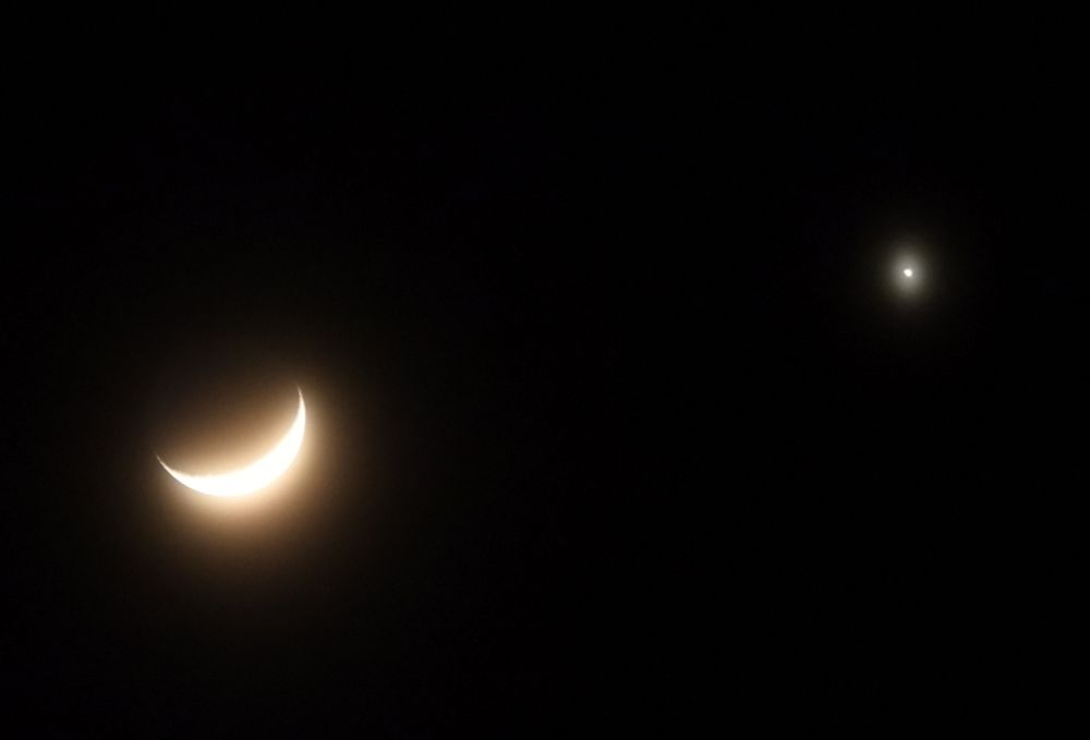 Crescent moon, with bright Venus to the right of her, shining with an amber hue in a slightly misty sky