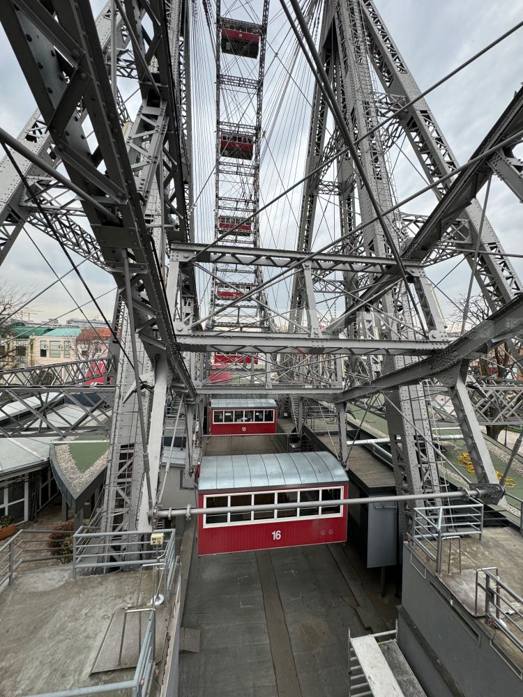 A photo of the red streetcar-like compartments and Eiffel-Tower-like metalwork of the Riesenrad (Ferris Wheel) in the Prater in Vienna