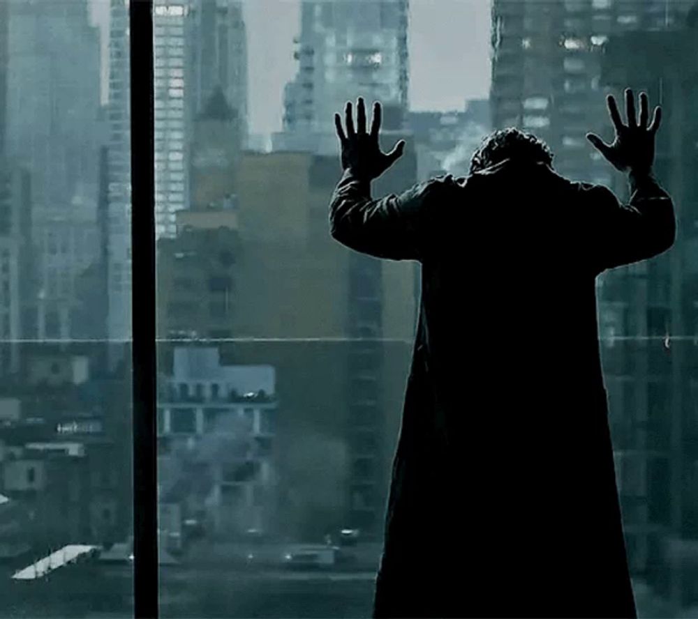 a man in a black coat is standing in front of a window with his hands up