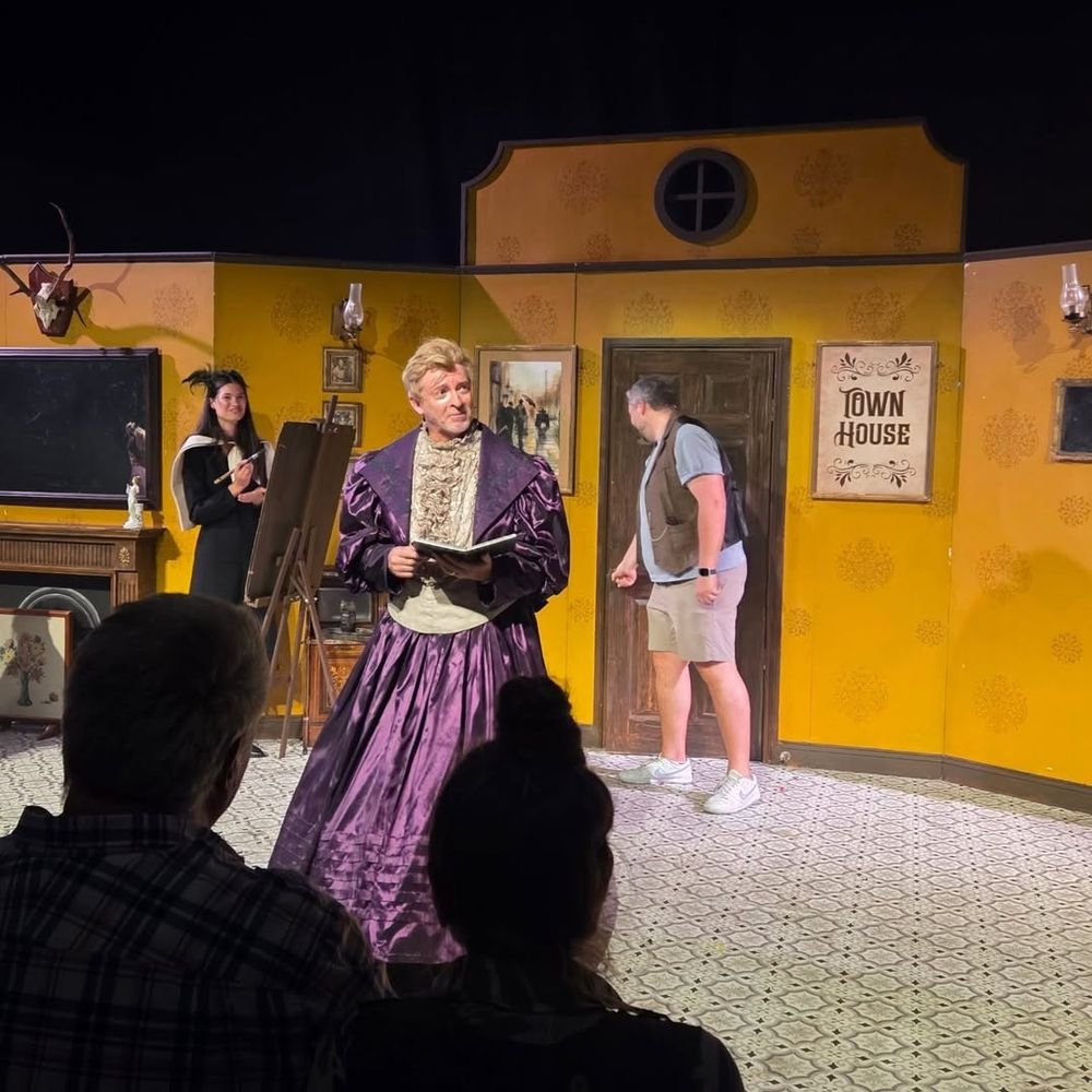 Rhys Darby in a purple Victorian style satin dress 