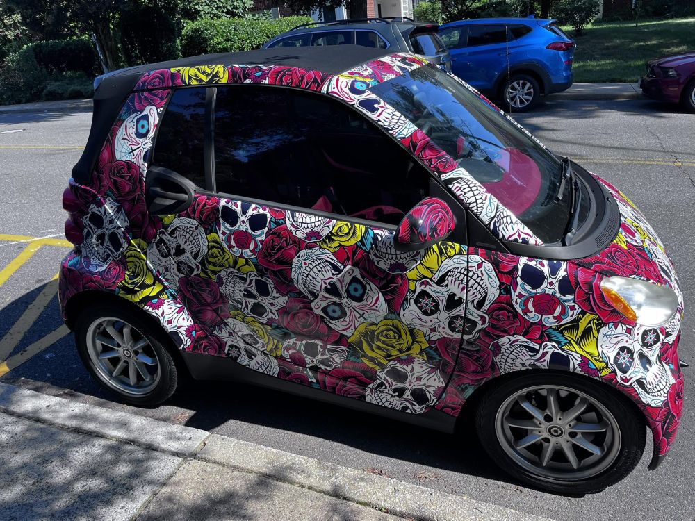 A very small car with a Dia de Los Muertos skulls wrap