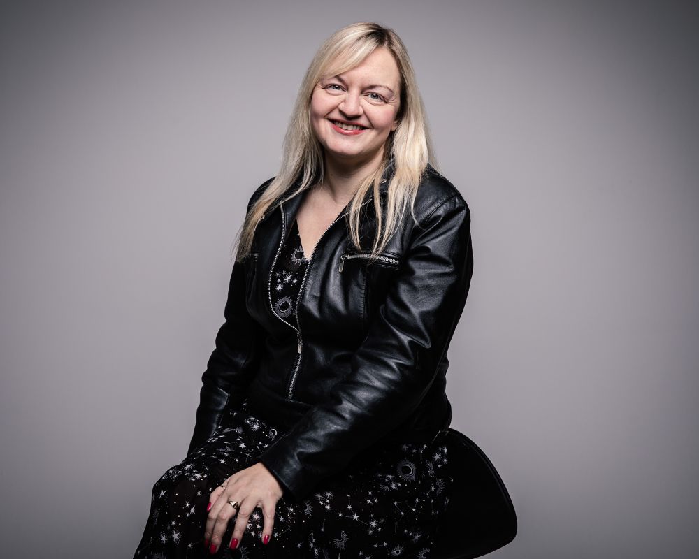 Headshot of Jo wearing a black leather jacket over a black dress with gold stars on 