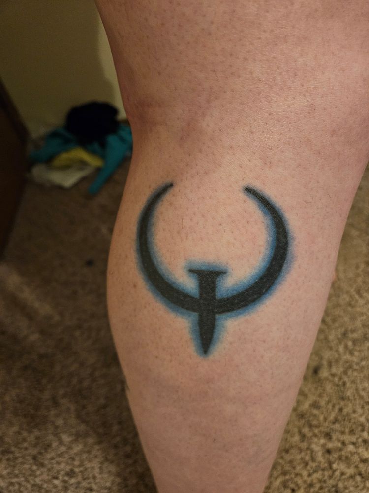A tattoo on the outside of Sabryna's leg of a black Quake logo, seemingly glowing blue as if with energy reminiscent of the Quad Damage power up from that series of games 