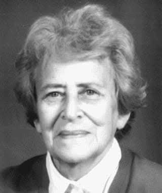 Fotografie zeigt Dora Schaul mit ergrautem, kurzem Haar in die Kamera blickend und lächelnd. Sie trägt ein weißes Hemd und einen Cardigan. Nachweis von wiki commons folgt. 
