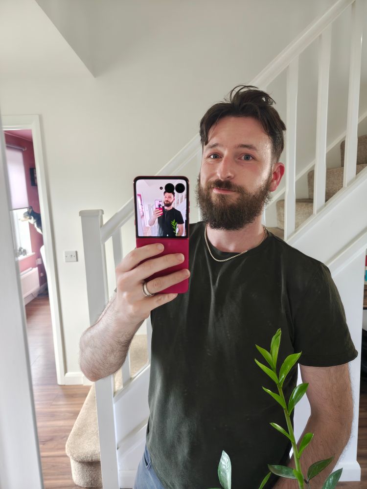 Rossy is standing in a green t-shirt holding a pink flip phone.