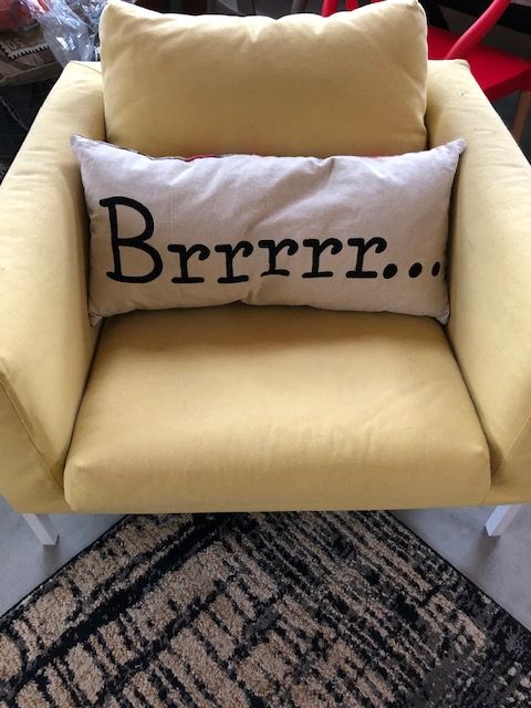 A yellow chair with a white pillow. The pillow has the word Brrrrrr,,, on it.