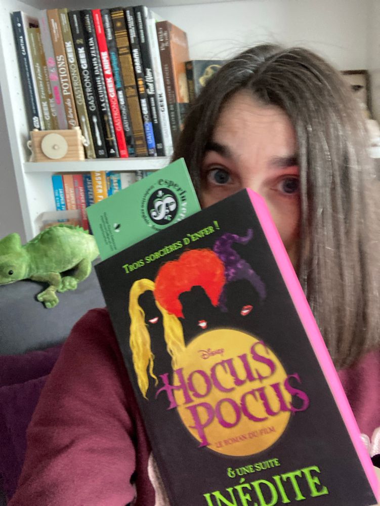 Personne devant une bibliothèque et qui tient le livre Hocud Pocus devant elle