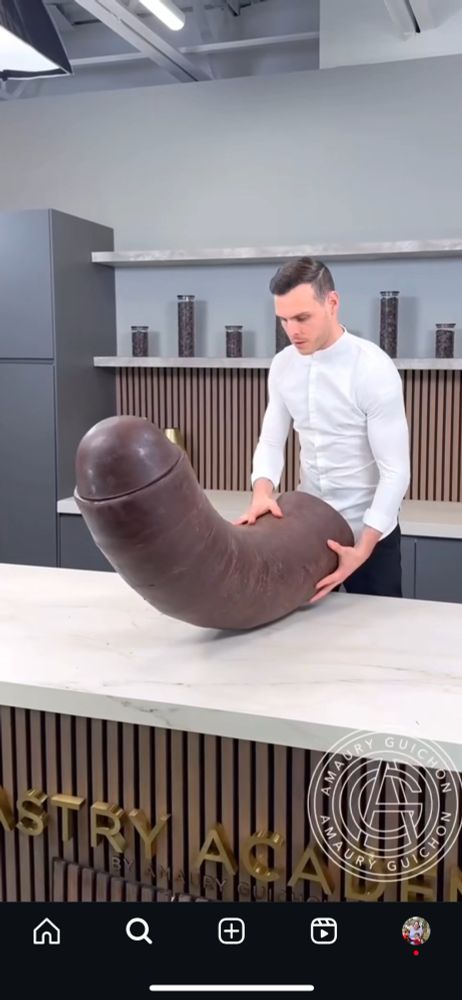 a man standing at a counter with an absolutely enormous chocolate penis 
