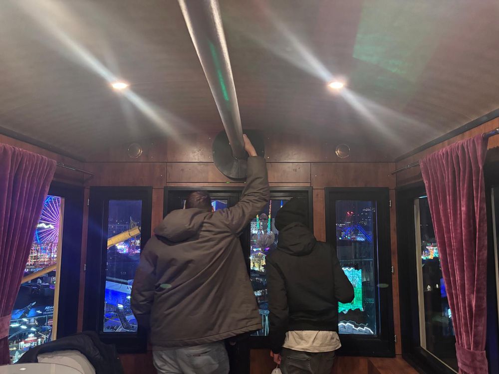 Jason und Mirco von hinten aus dem Fenster schauend in einer Riesenrad-Gondel, dahinter der bunt beleuchtete Wiener Prater 