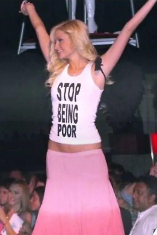 Paris Hilton con los brazos extendidos para que se lea bien su camiseta: Stop being poor