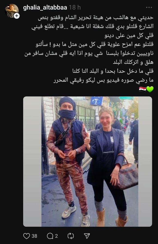 smiling estern style dressed young woman with HTS young man in battle dress and sneakers, carrying a weapon, covering his face